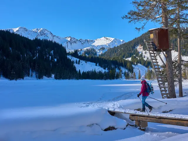 Ältere Frau mit Schneeschuhen beim Wandern durch die verschneite Berglandschaft des Kleinwalsertals in Vorarlberg.