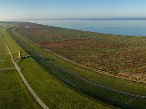 alt="Blick von oben auf den Nordseedeich mit dem Pilsumer Leuchtturm, Ostfriesland"