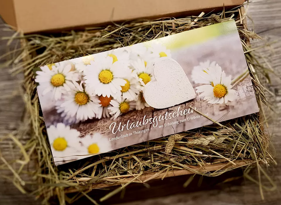 Urlaubsgutschein Blütenherz im mit Heu gefüllten Geschenkkarton 