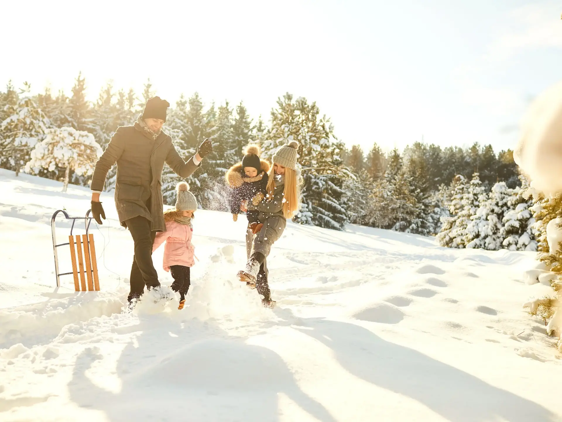 Familie tobt im Schnee mit Holzschlitten.