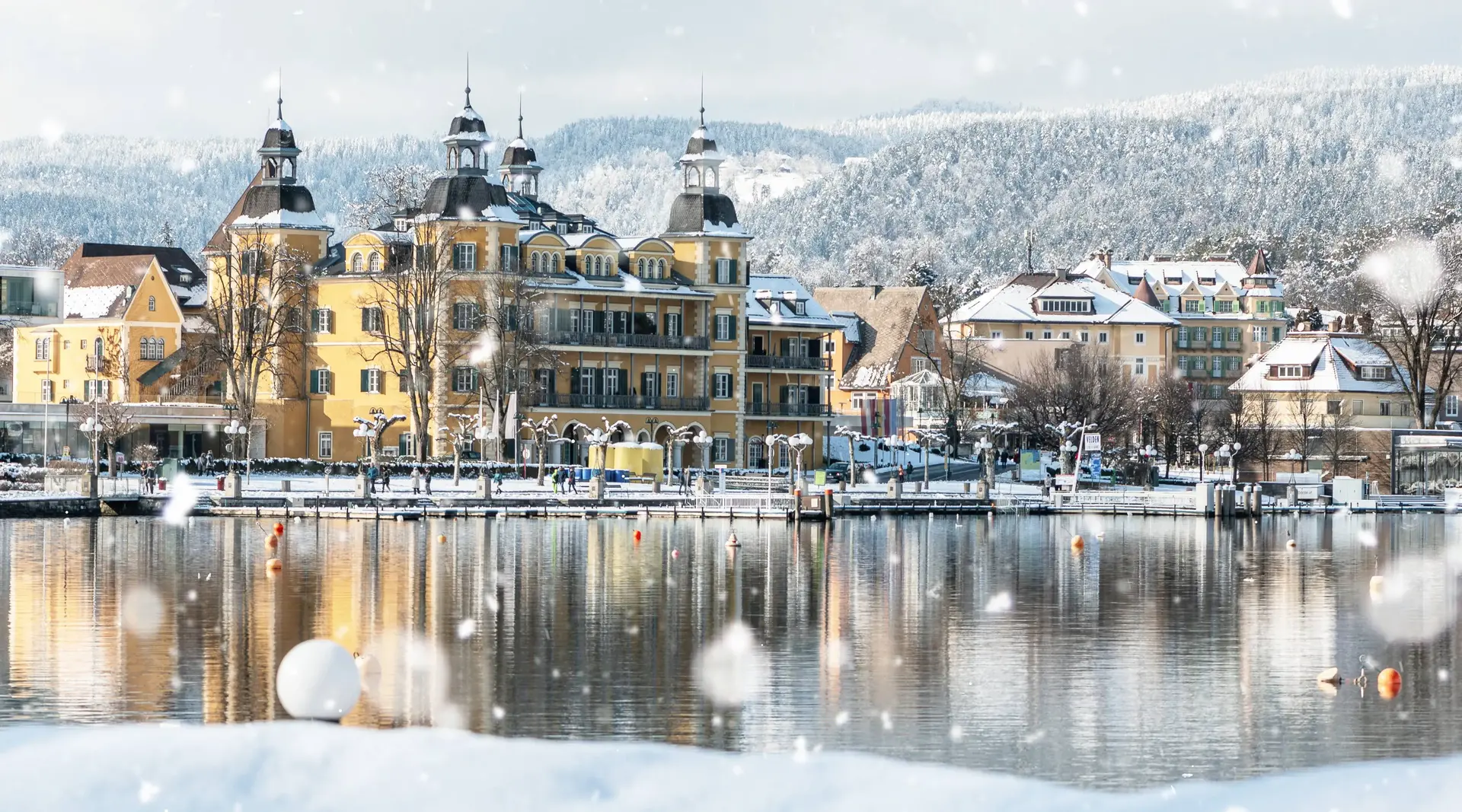 Velden am Wörthersee – Wintermärchen in Kärnten erleben Verschneites Schloss Velden am Wörthersee mit winterlicher Uferpromenade in Kärnten.