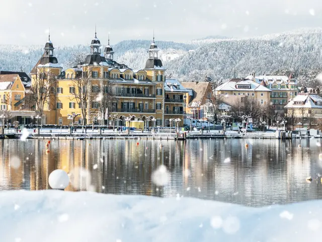 Velden am Wörthersee – Wintermärchen in Kärnten erleben Verschneites Schloss Velden am Wörthersee mit winterlicher Uferpromenade in Kärnten.