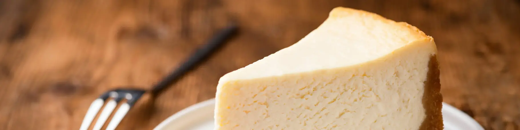 Cheesecake slice, New York style classical cheese cake on wooden background. Slice of tasty cake on white plate served with dessert fork