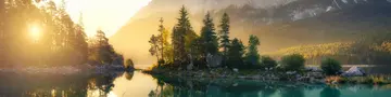 Idyllischer See bei Sonnenaufgang, ein malerisches Panorama mit majestätischen Bergen und dem goldenen Sonnenlicht, das hinter den Bäumen hereinscheint