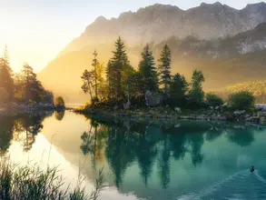 Idyllischer See bei Sonnenaufgang, ein malerisches Panorama mit majestätischen Bergen und dem goldenen Sonnenlicht, das hinter den Bäumen hereinscheint
