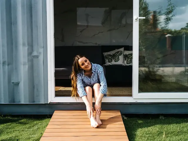 Frau sitzt an geöffneter Glastüre eines Tiny Houses.