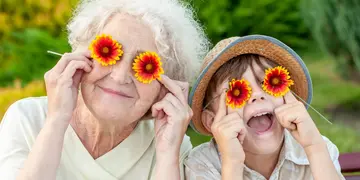 Boy and grandmother puts on the eyes of chamomile. Family holiday.Laughing grandson with his beloved grandmother spend leisure time outdoors. An elderly woman and a grandchild. Summer spring time Boy and grandmother puts on the eyes of chamomile. Family holiday.Laughing grandson with his beloved grandmother spend leisure time outdoors. An elderly woman and a grandchild. Summer spring time