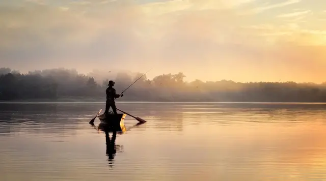 Angler auf einem ruhigen See bei Sonnenaufgang