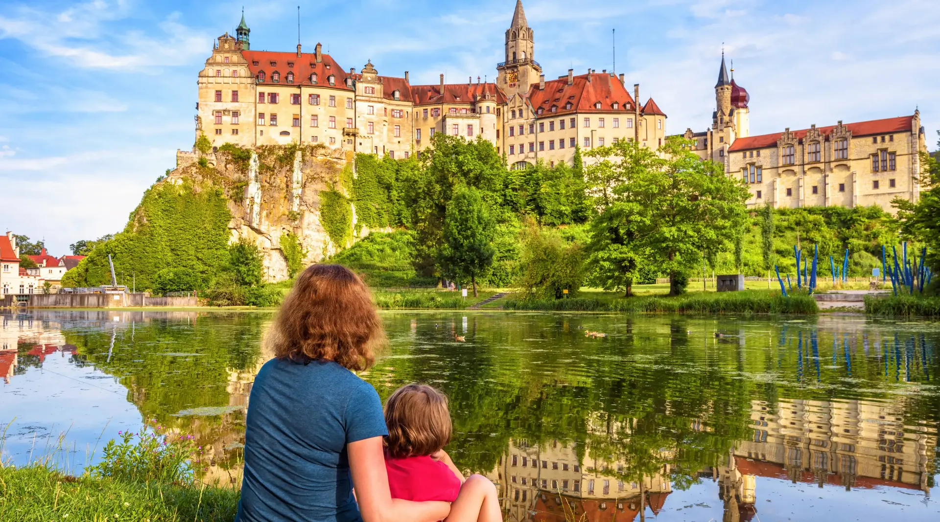 Familienausflug nach Sigmaringen – Schloss und Donau erleben - © scaliger, Adobe Stock Mutter und Kind sitzen im Sommer an der Donau mit Blick auf Schloss Sigmaringen in Baden-Württemberg.