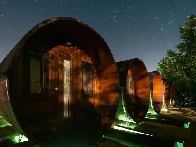 Beleuchtete Holz-Weinfässer als Ferienunterkünfte bei Nacht unter Sternenhimmel
