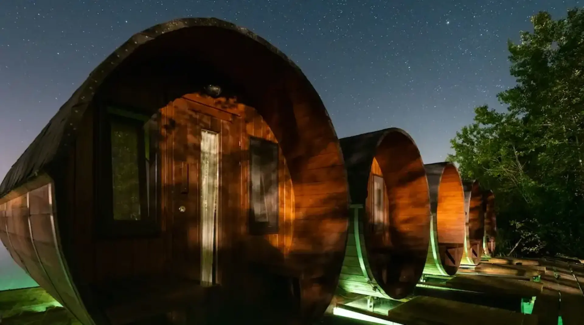 Beleuchtete Holz-Weinfässer als Ferienunterkünfte bei Nacht unter Sternenhimmel