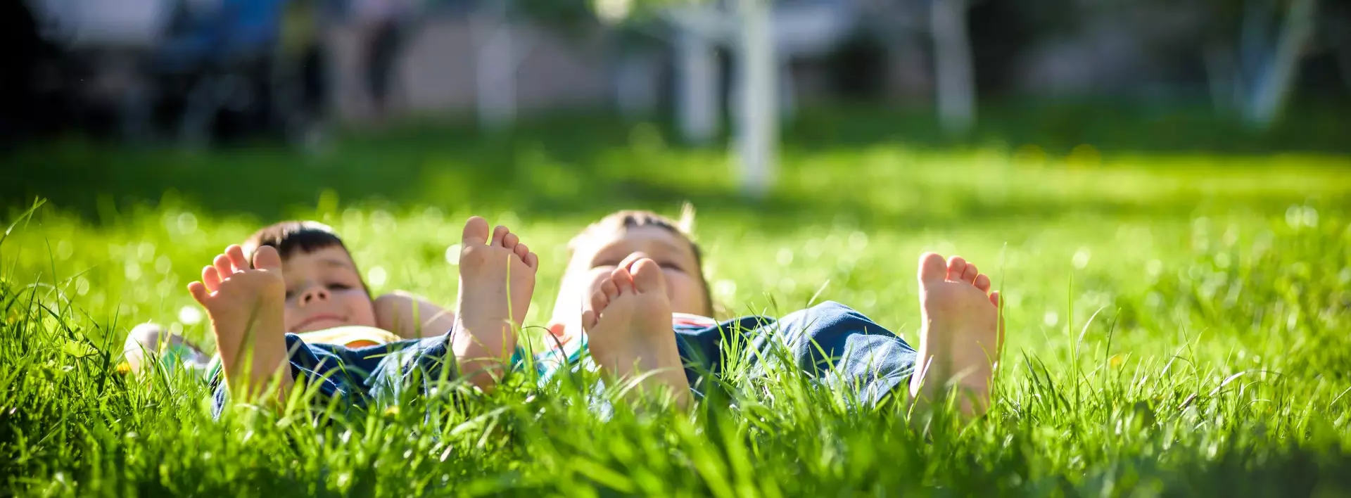 Zwei Jungen liegen auf dem Rücken mit nackten Füßen auf einer Wiese im Gras 