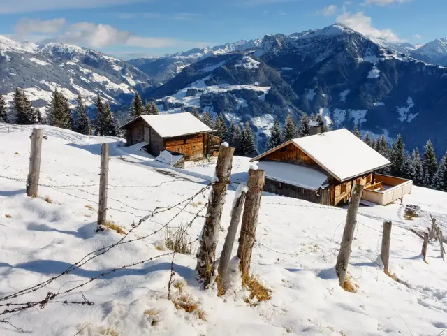 Verschneite Almhütten in den Bergen mit Alpenpanorama und Winterlandschaft.
