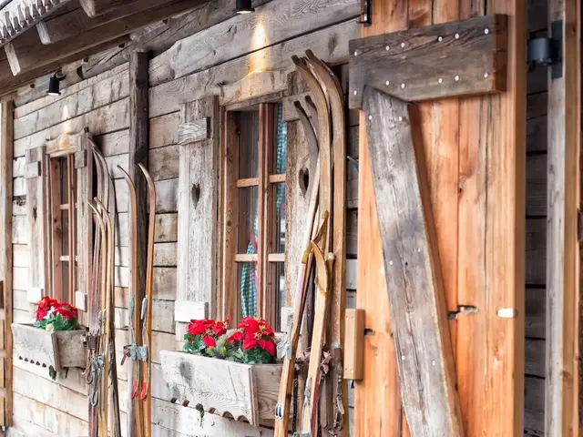 Rustikale Berghütte mit Holzfassade und Skiern im Winter Holzfassade einer rustikalen Berghütte mit alten Skiern und Blumenkästen am Fenster im Winter