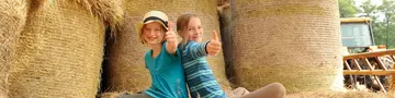 Kinder im Heu - © Susanne Mölle Zwei glückliche Mädchen sitzen auf Heuballen in der Scheune und halten ihre Daumen nach oben