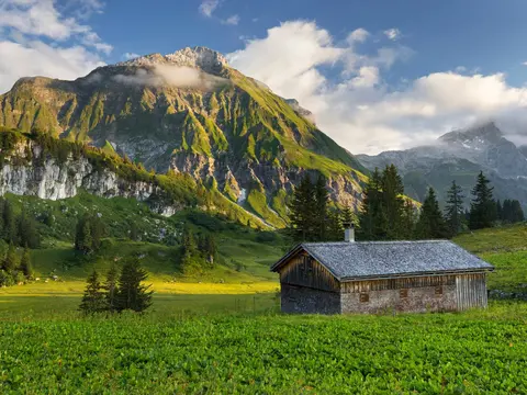alt="Gemütliche Holzhütte vor der imposanten Juppenspitze im Lechquellengebirge, Vorarlberg, Österreich – alpine Idylle inmitten der Natur."