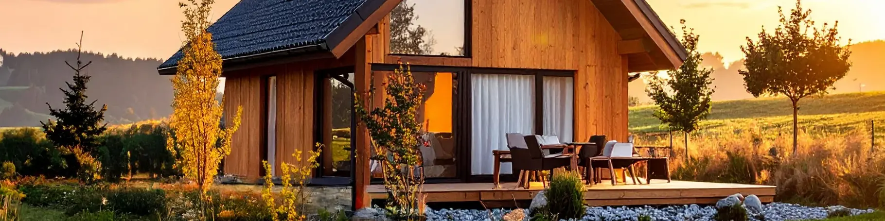 Kleines modernes Ferienhaus auf dem Land mit Holzschirm im orangen Abendlicht.