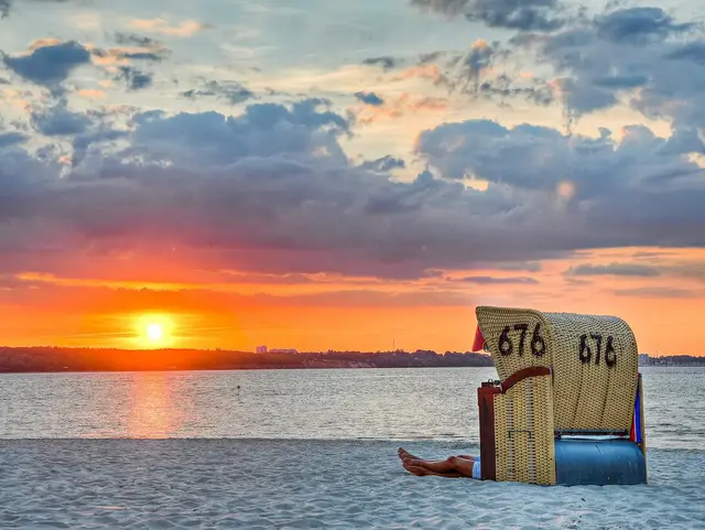 Romantischer Sonnenuntergang im Strandkorb – Ferienwohnung auf Fehmarn Ein Paar sitzt im Strandkorb am Strand von Fehmarn und erlebt gemeinsam den Sonnenuntergang.