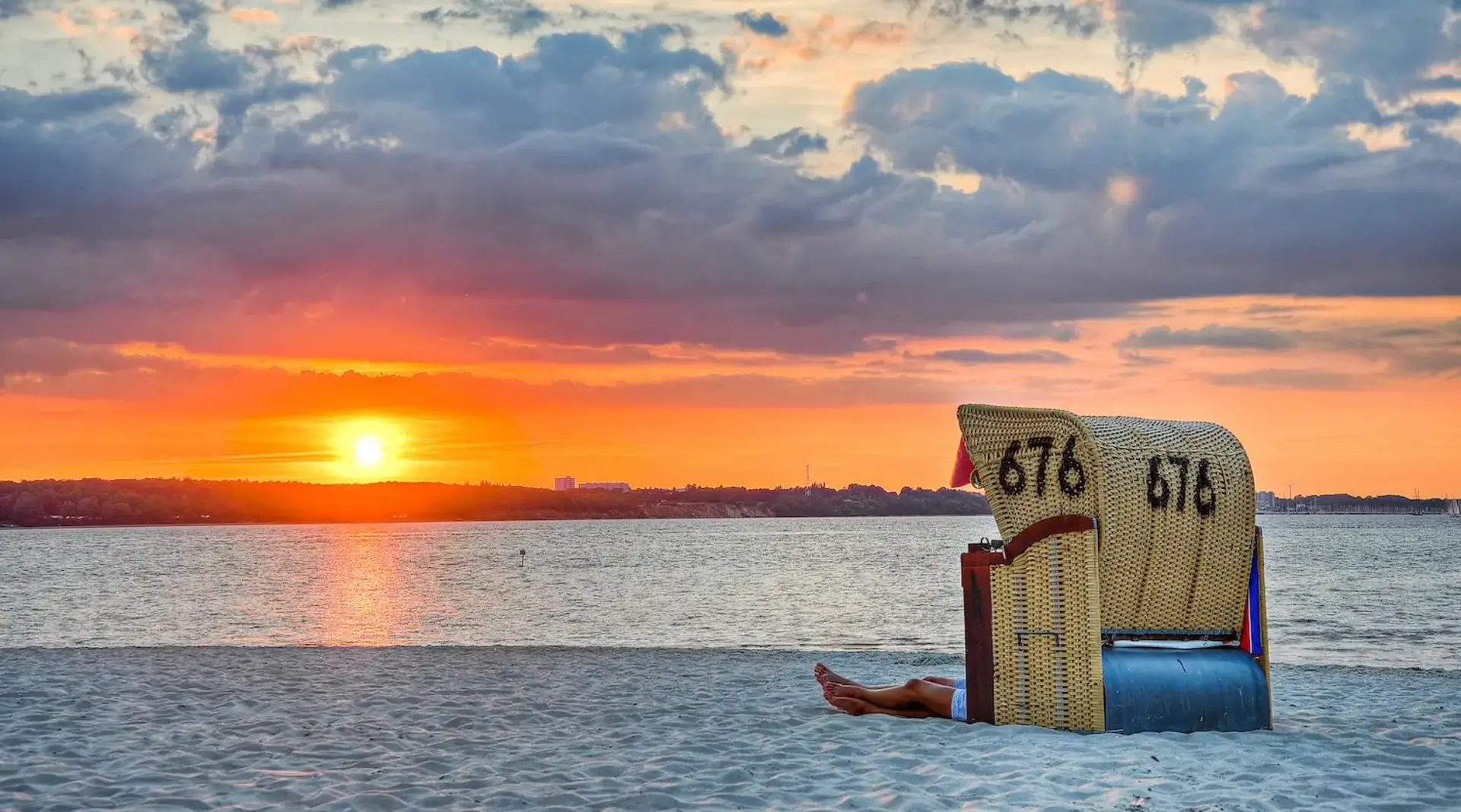 Ein Paar sitzt im Strandkorb am Strand von Fehmarn und erlebt gemeinsam den Sonnenuntergang. 