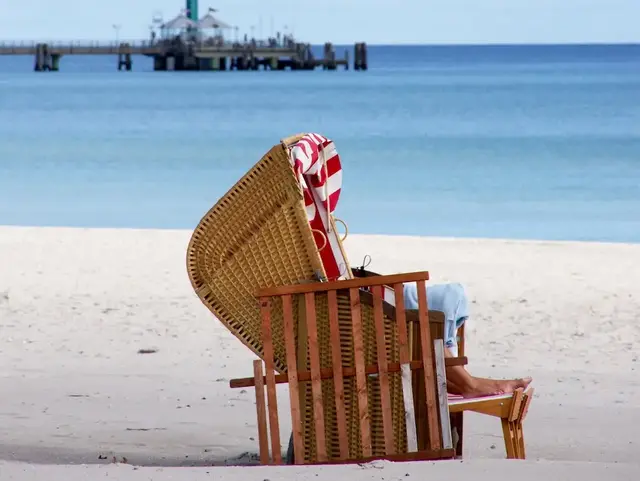Ein Strandkorb steht am Strand von Grömitz mit der Seebrücke im Hintergrund an der Ostsee. 