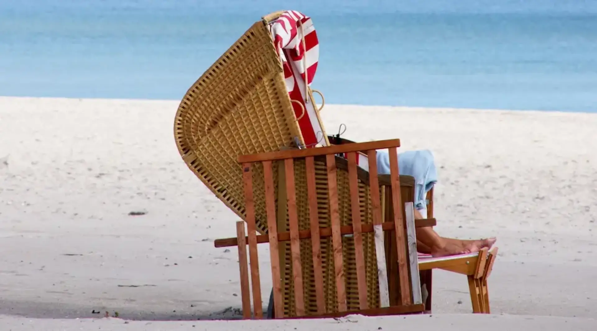 Ein Strandkorb steht am Strand von Grömitz mit der Seebrücke im Hintergrund an der Ostsee. 