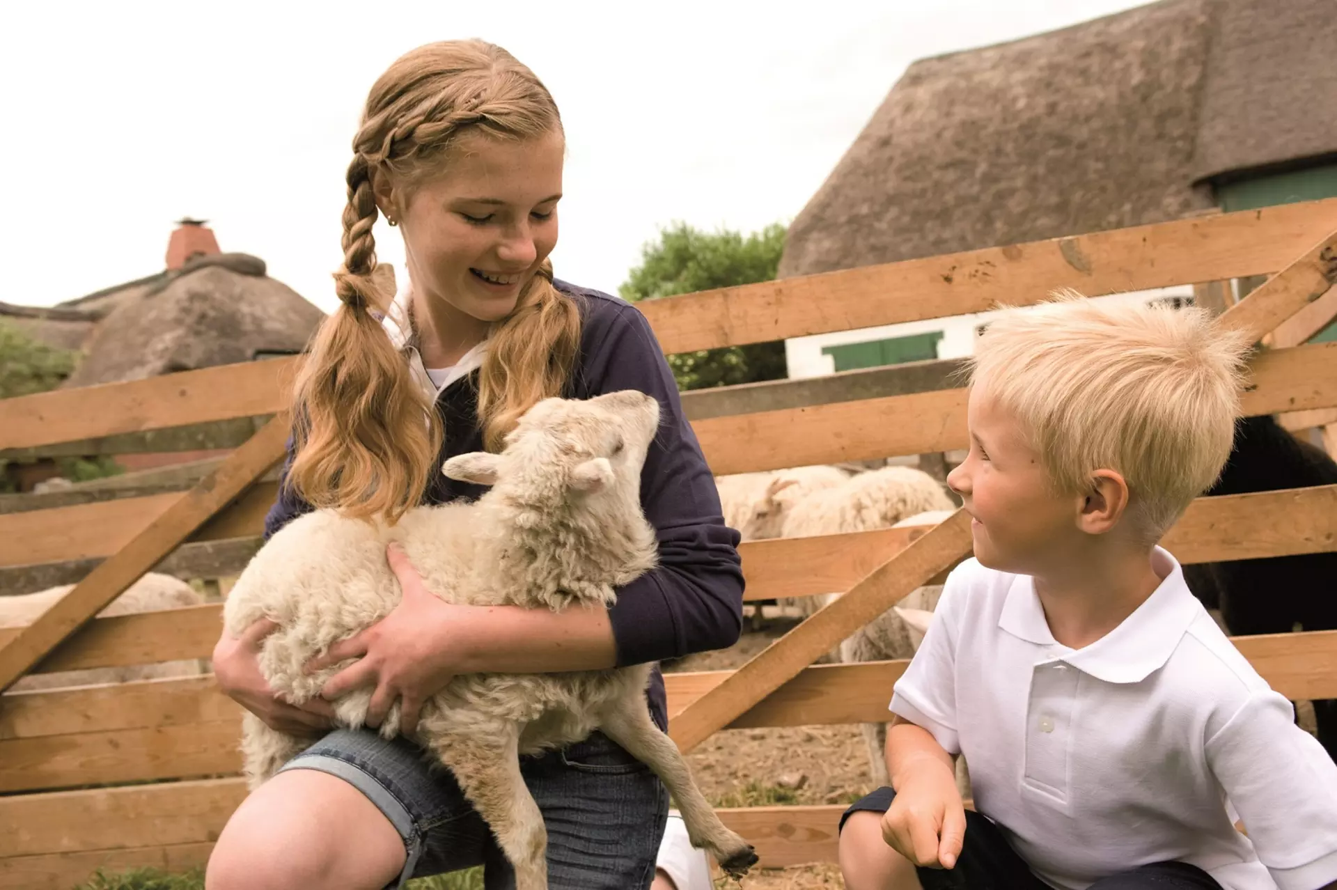 Zwei Kinder kümmern sich um ein Lamm bei Ihrem Urlaub auf dem Bauernhof in Schleswig-Holstein.