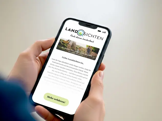Zwei Hände halten ein Smartphone mit dem Landsichten Newsletter voller Inspirationen für Urlaub auf dem Land.