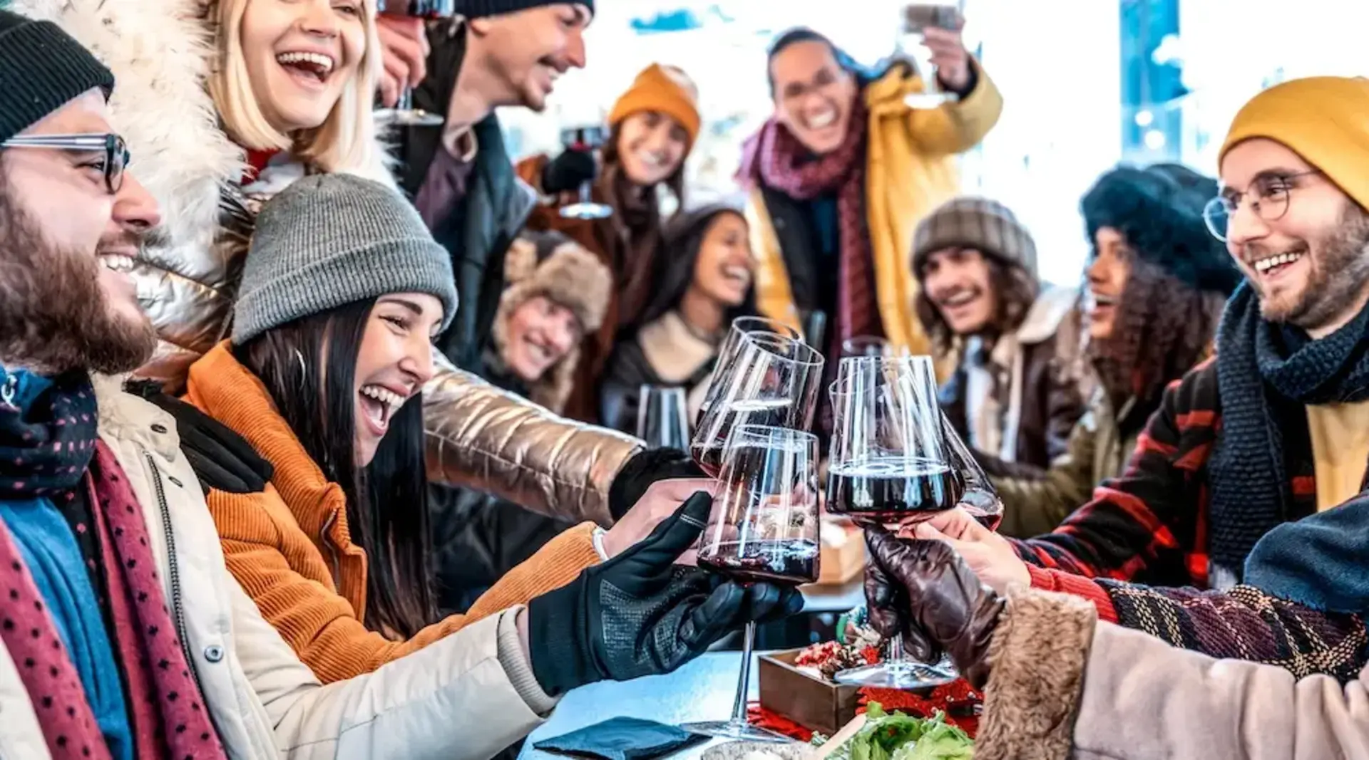 Gruppe junger Freunde stößt mit Rotwein auf der Terrasse einer Berghütte im Winter an