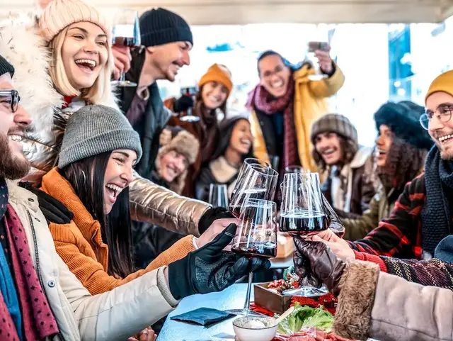 Gruppe junger Freunde stößt mit Rotwein auf der Terrasse einer Berghütte im Winter an