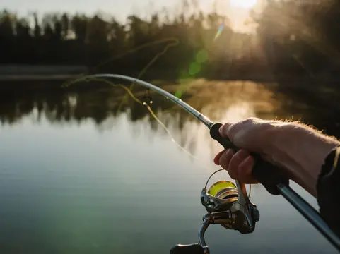 alt="Fisherman with rod, spinning reel on the river bank. Sunrise. Fishing for pike, perch, carp. Fog against the backdrop of lake. background Misty morning. wild nature. The concept of a rural getaway."