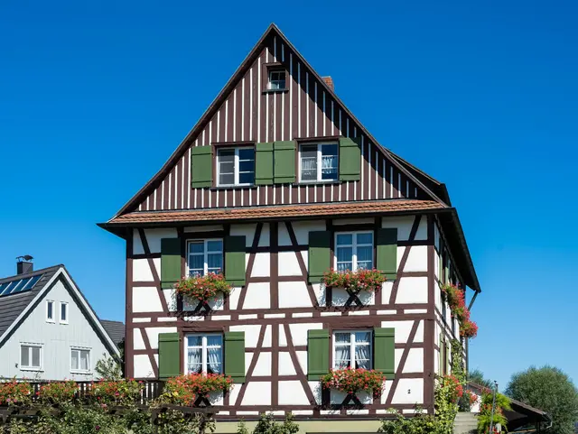 Das „Hohe Haus“ in Mittelzell auf der Insel Reichenau Das „Hohe Haus“, ein Fachwerkbau aus dem 17./18. Jahrhundert im Ortsteil „Im Weiler“ in Mittelzell auf der Insel Reichenau im Bodensee im Landkreis Konstanz in Baden-Württemberg. Grüne Klappläden, Blumenschmuck und blauer Himmel.