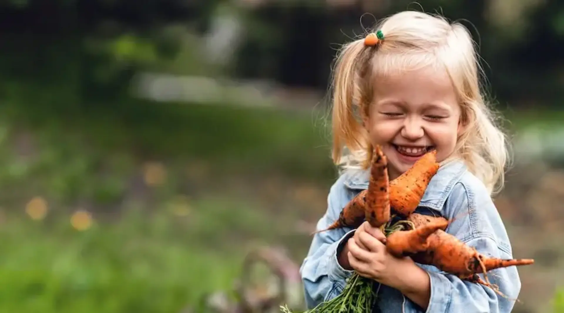 Glück auf dem Land – Holsteinische Schweiz Bauernhof Urlaub  Ein lachendes Mädchen hält frisch geerntete Karotten auf einem Bauernhof während eines Urlaubs in der Holsteinischen Schweiz.